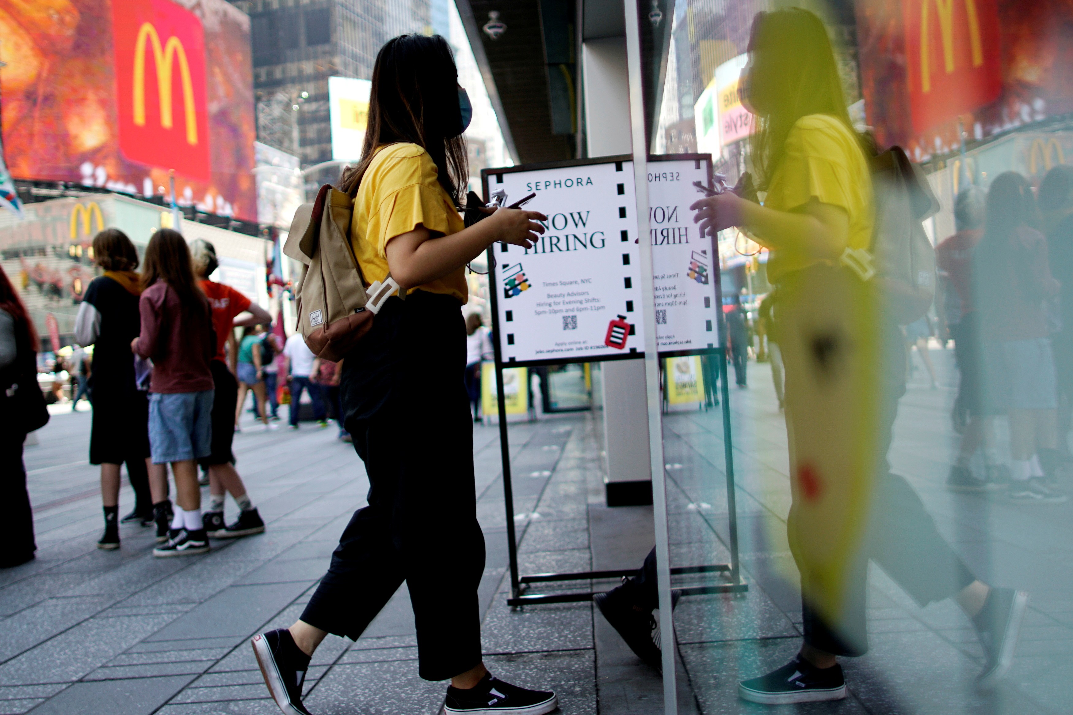 Mulher entra em loja ao lado de uma placa anunciando vagas de emprego na Times Square em Nova York, EUA
